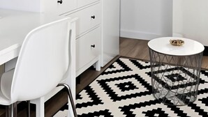 Een moderne keuken met witte kasten, een koffieapparaat en een waterkoker. Er staat een klein, rond tafeltje met een decoratieve schaal.