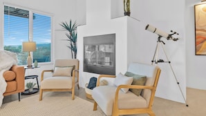 A modern living room with a large window, two wooden chairs, a sofa, a telescope, and a framed picture on the wall.