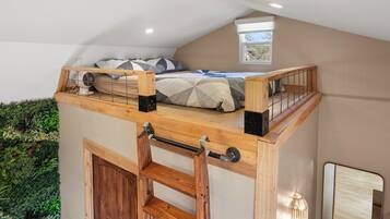Un dormitorio tipo loft con una cama litera, un ventanal pequeño y una escalera de madera.