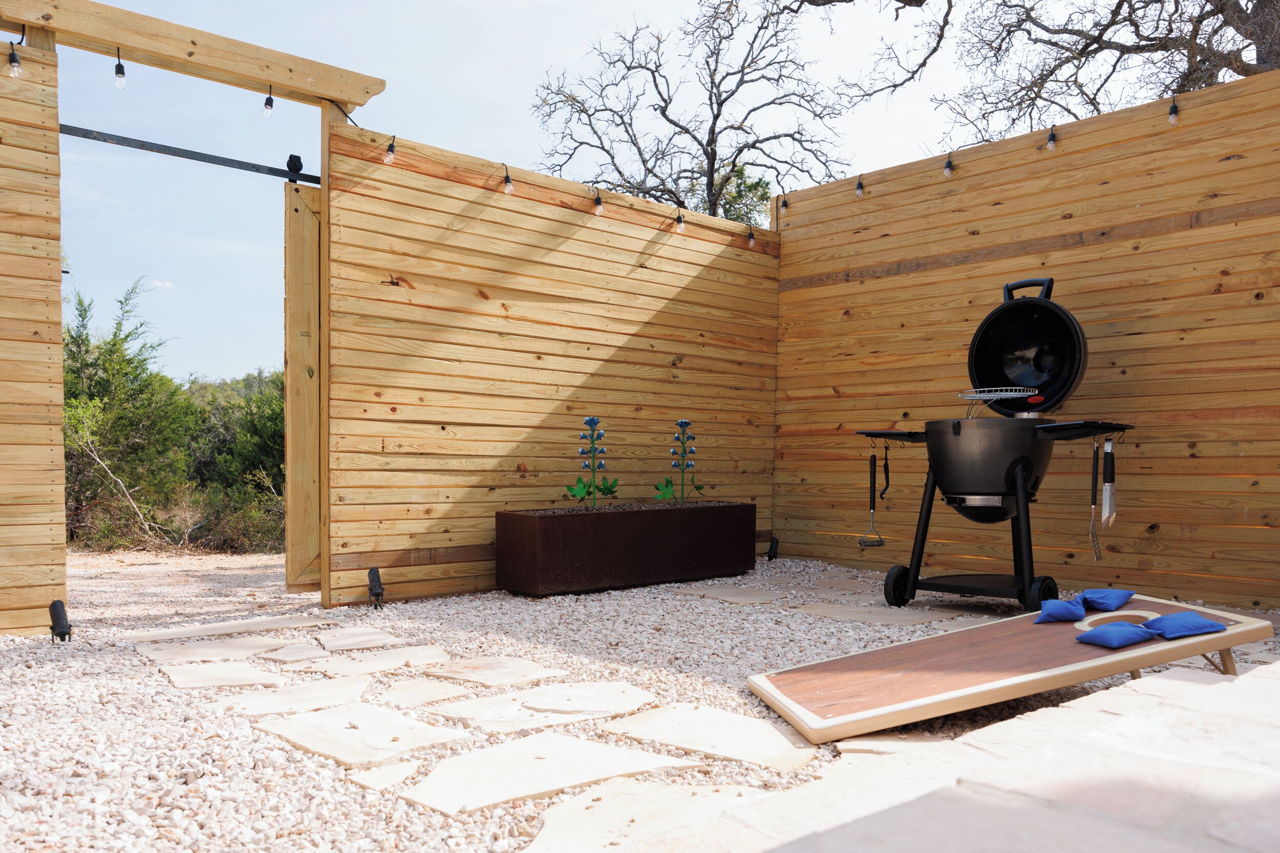 Un patio exterior de madera con una parrilla, una maceta con plantas y un piso de madera.