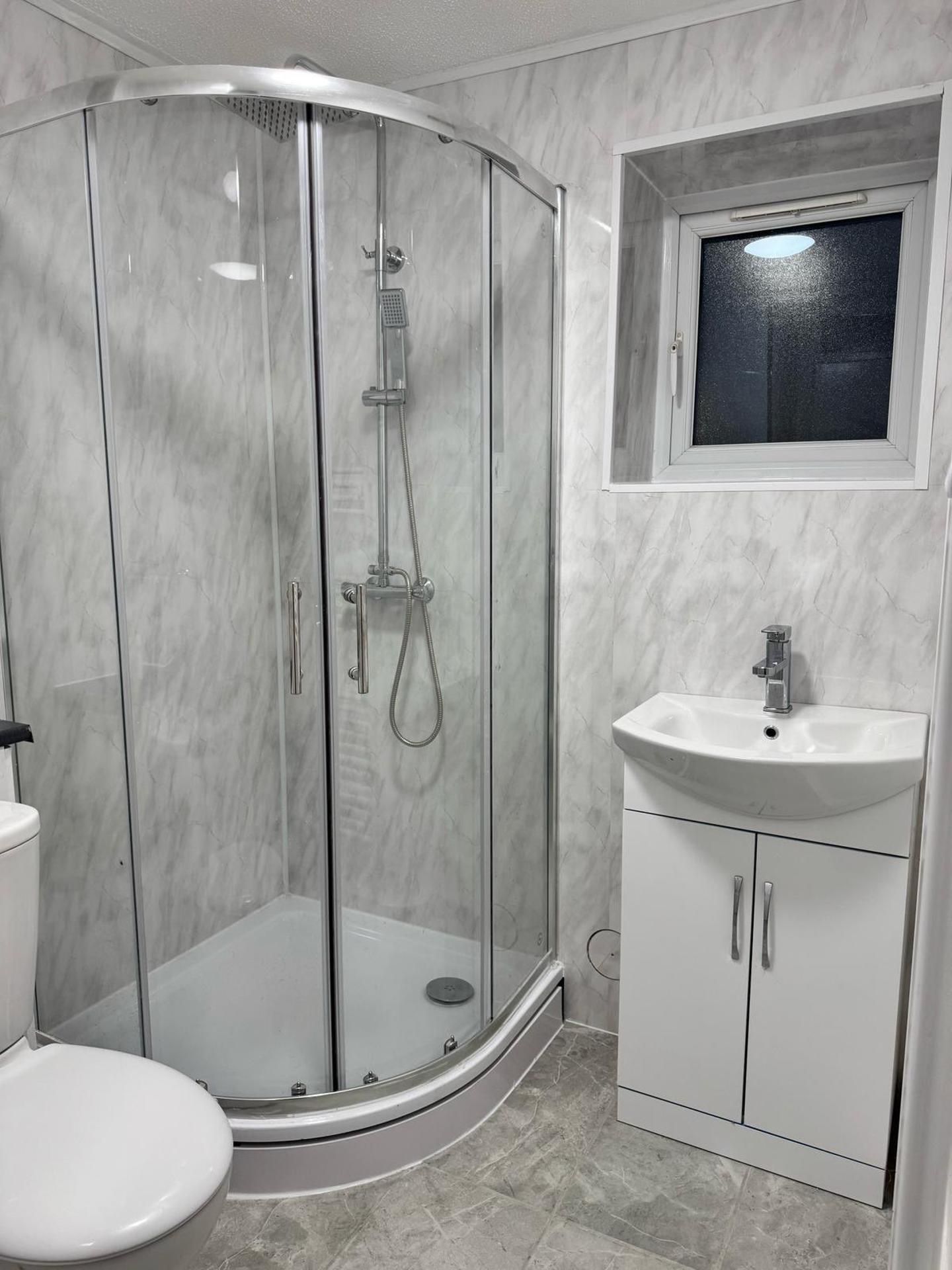 A modern bathroom with a glass-enclosed shower, a sink with a window above, and a toilet.