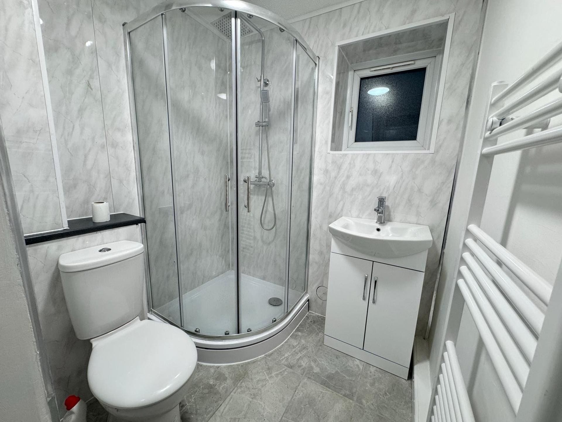 A bathroom with a glass-enclosed shower, a toilet, a sink, and a window above the sink.