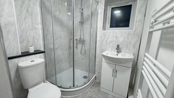 A bathroom with a glass-enclosed shower, a toilet, a sink, and a window above the sink.