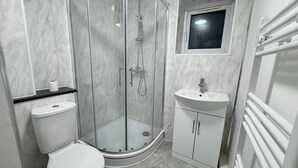 A modern bathroom with a glass-enclosed shower, a toilet, a sink, and a small window above the sink.