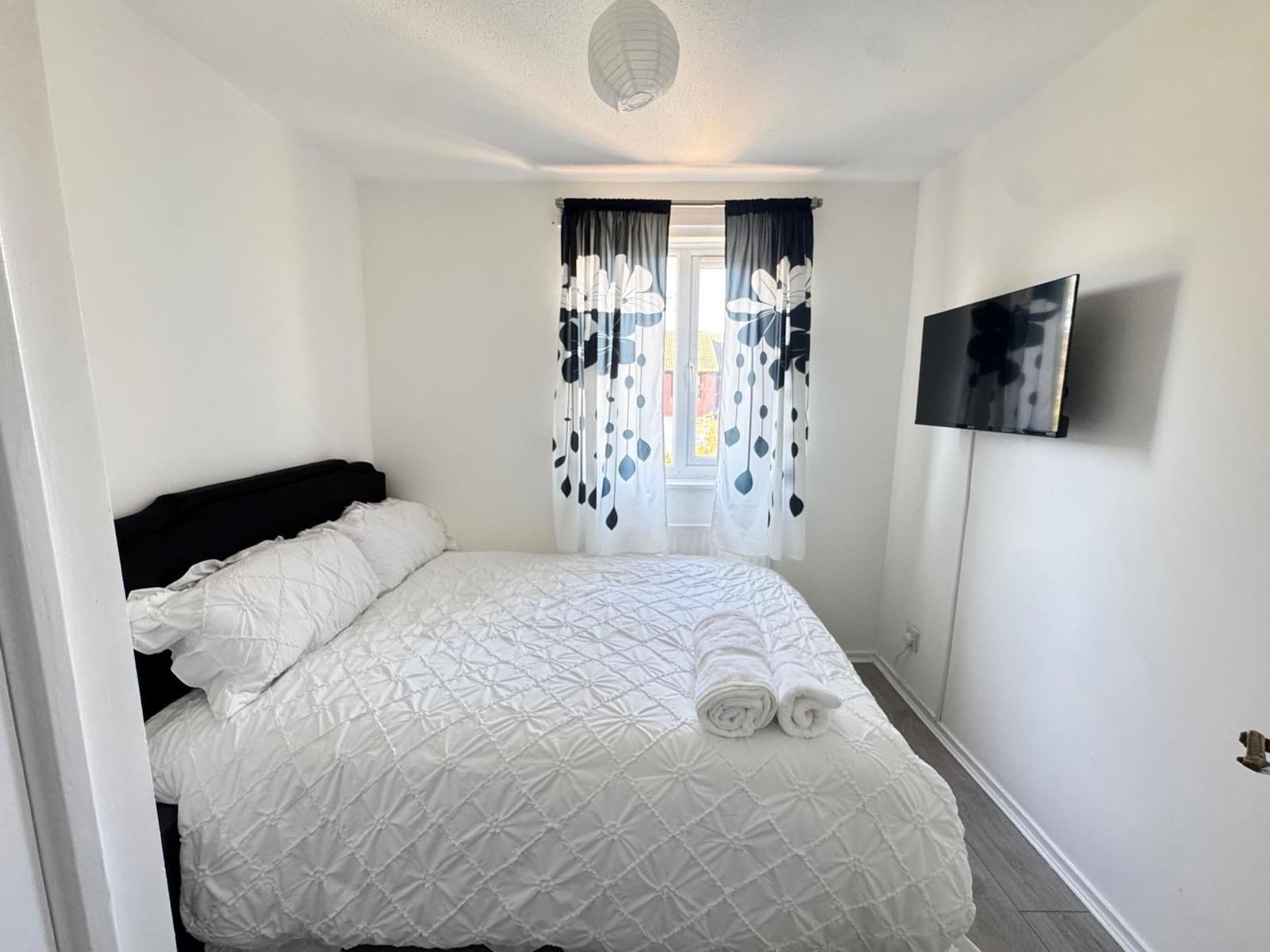 A bedroom with a bed, curtains, a television, and a door.