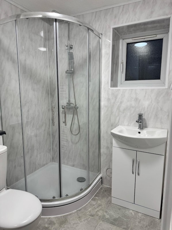 A modern bathroom with a glass-enclosed shower, a white sink, and a toilet. - Charming London Apartment Retreat (London)