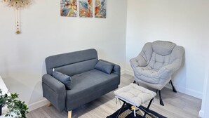 A modern living room with a grey sofa, a grey armchair, and a small ottoman. There are three floral wall art pieces above the sofa.