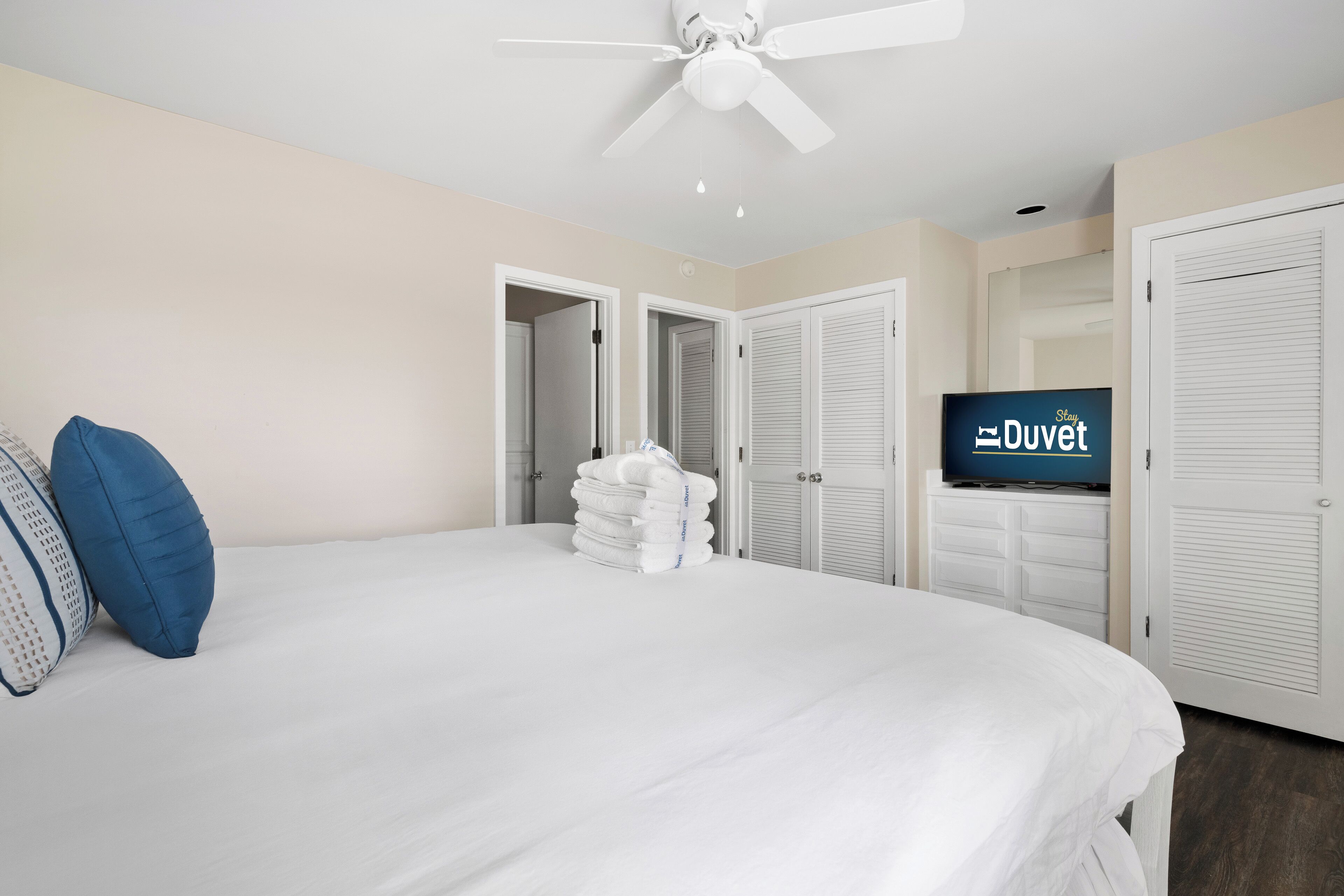 Een hotelkamer met een bed, een plafondventilator, een televisie en een stapel handdoeken.