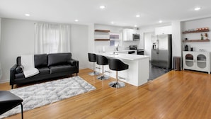 Un salon moderne avec un canapé en cuir noir, un tapis blanc et un plancher en bois.