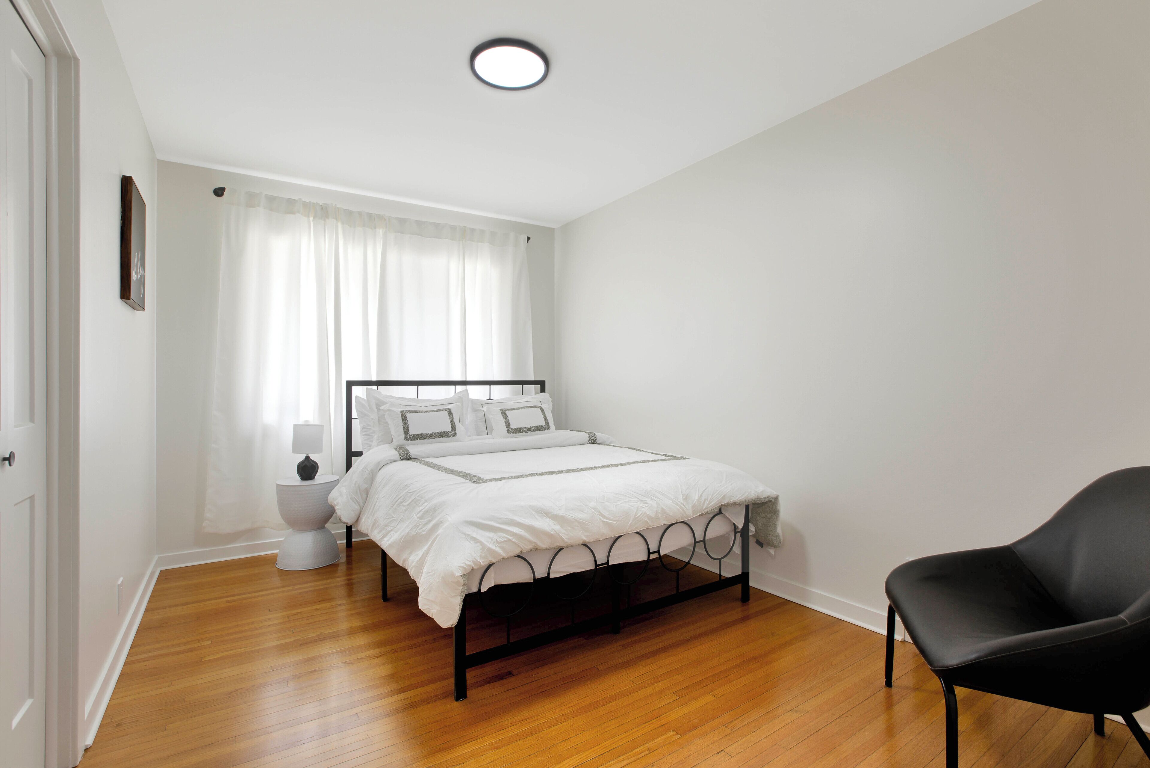 A bedroom with a bed, a chair, a bedside table, and a window with curtains.