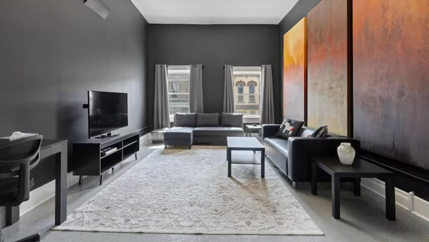 A modern living room with a large TV, a sofa, a coffee table, and a rug. - Spacious Luxury Black Downtown Apartment - Minutes from WEC! (Wilmington)