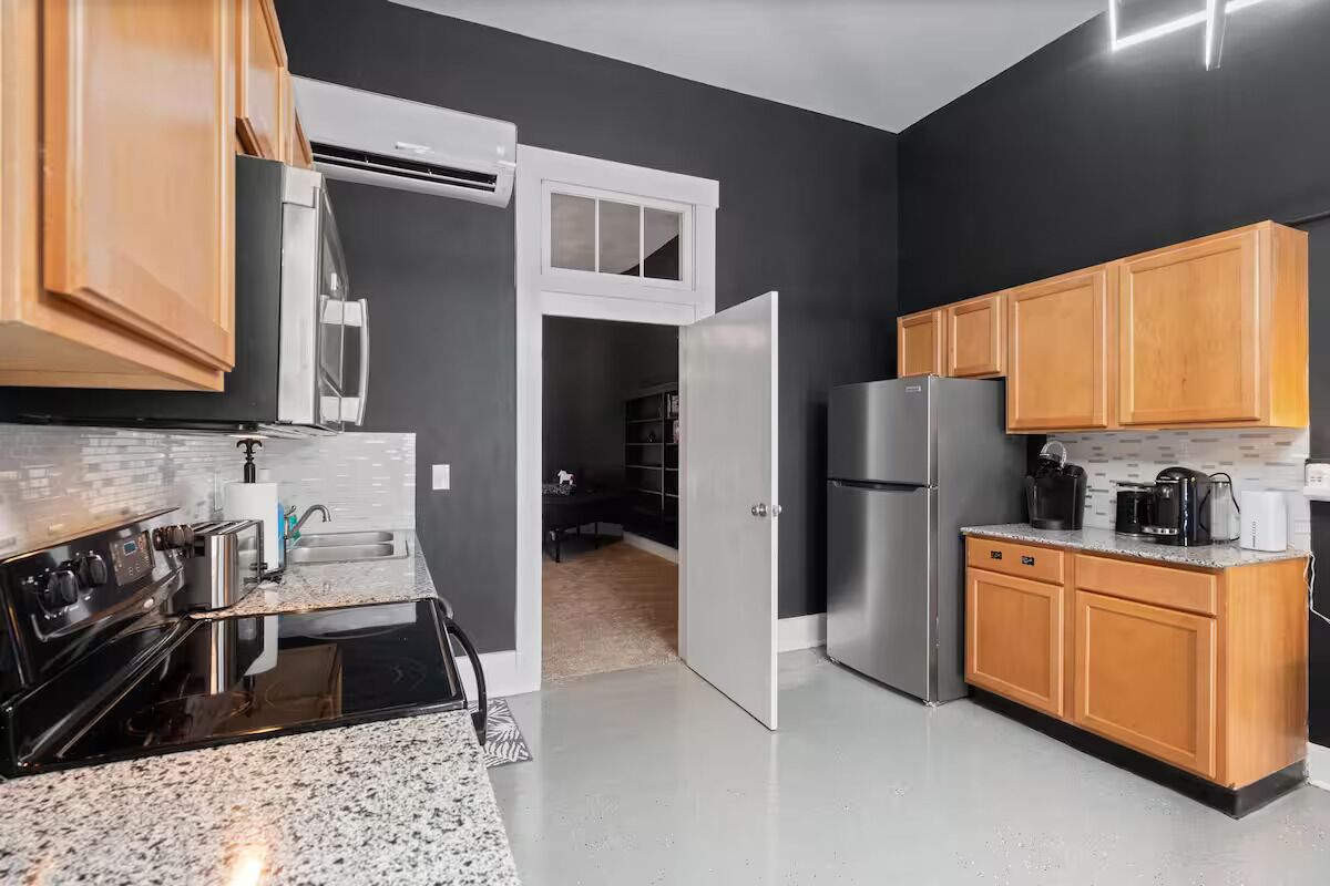 A modern kitchen with a black backsplash, wooden cabinets, stainless steel appliances, and a granite countertop.