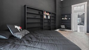 A modern bedroom with a large bed, a built-in bookshelf, and a view of the living area. - Spacious Luxury Black Downtown Apartment - Minutes from WEC! (Wilmington)
