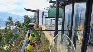 A balcony with a glass railing, potted plants, and a chair. - Glamping altos de la rivera (Jenesano)