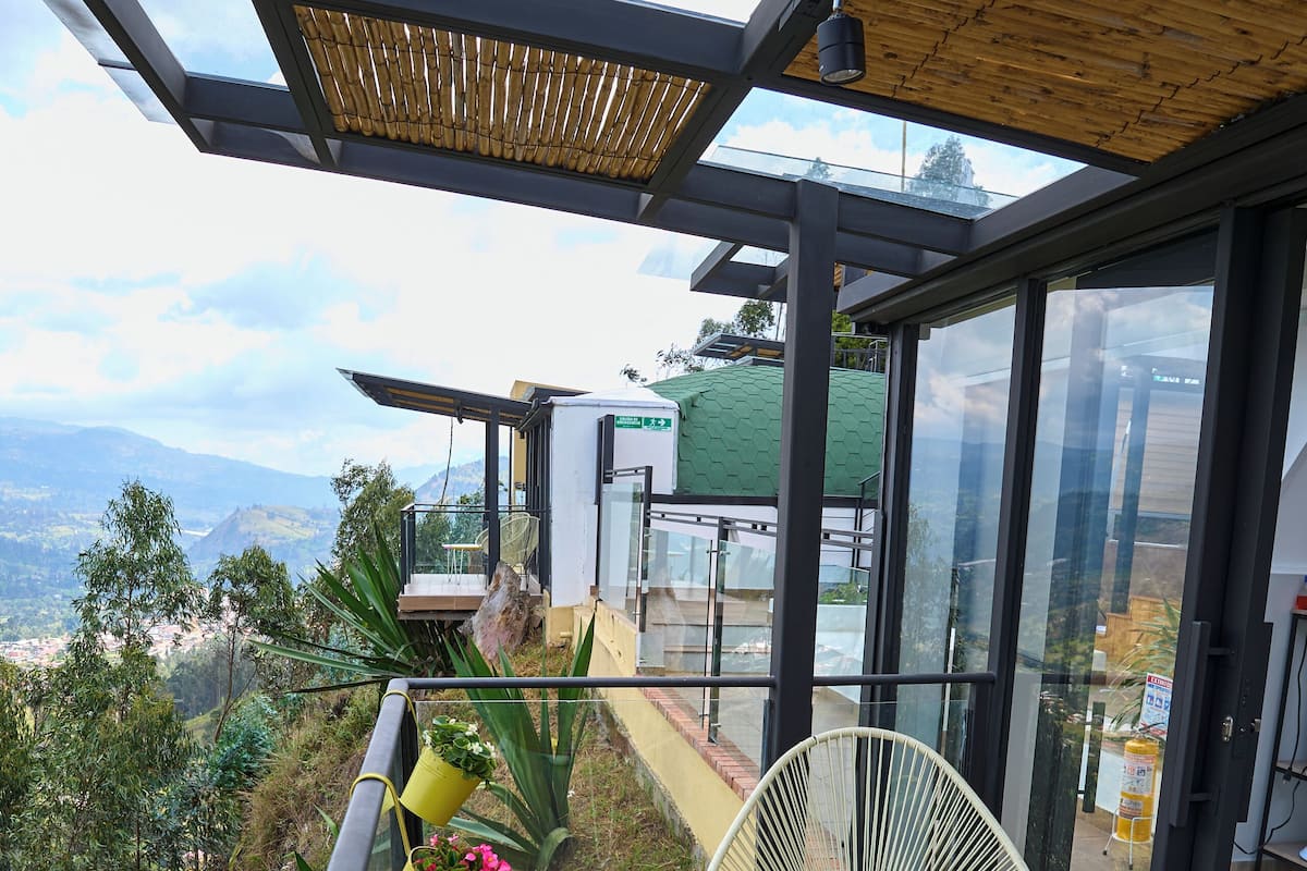 Un balcon doté d’une balustrade en verre, de plantes en pot et d’une chaise.