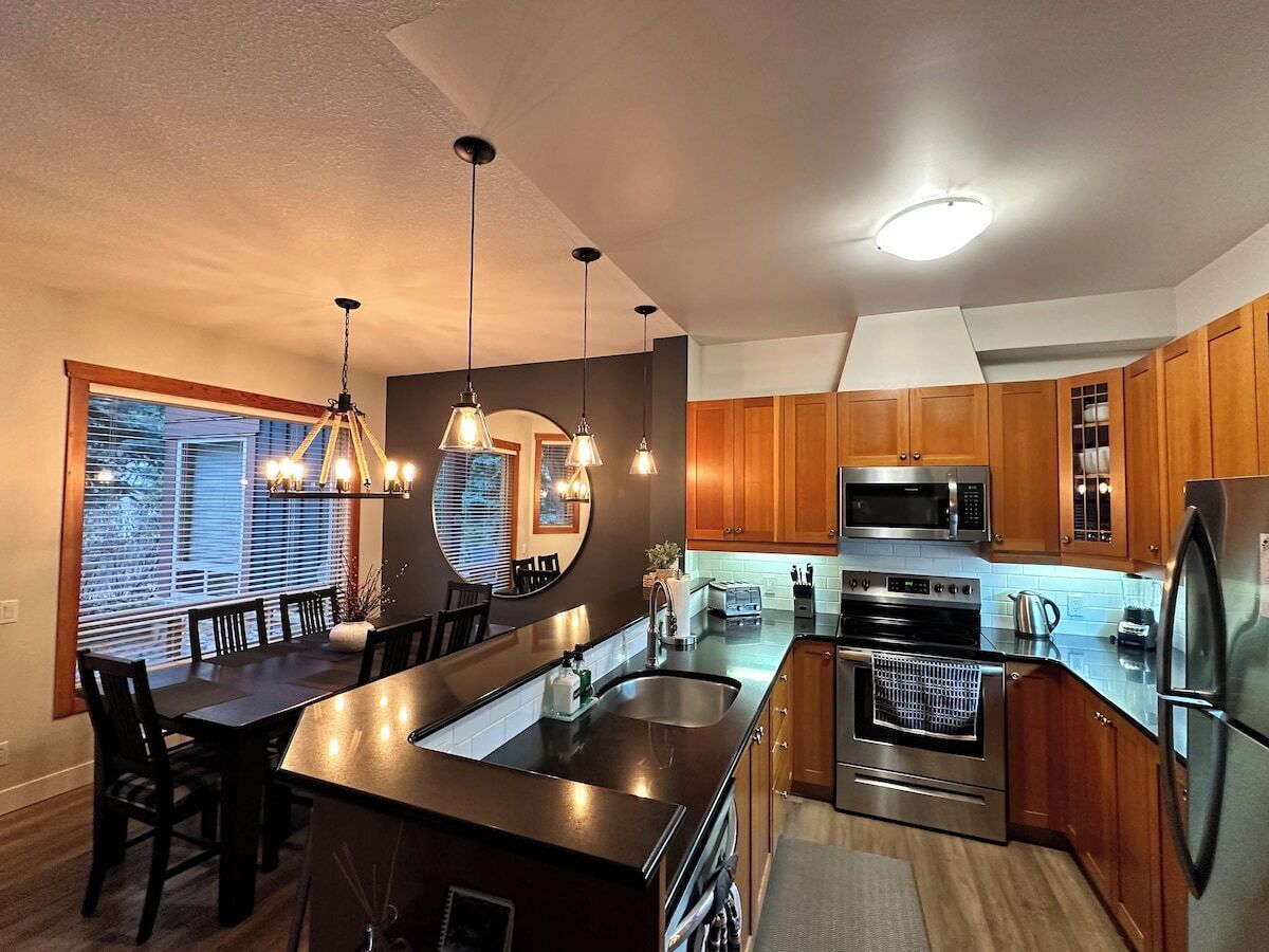Une cuisine moderne avec des meubles en bois, des appareils électroménagers en acier inoxydable et des luminaires suspendus.