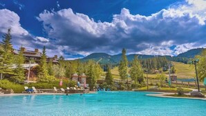A swimming pool with lounge chairs, surrounded by trees and a mountainous landscape.