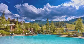 Une piscine entourée de chaises longues, bordée d’arbres et offrant une vue sur un paysage montagneux.