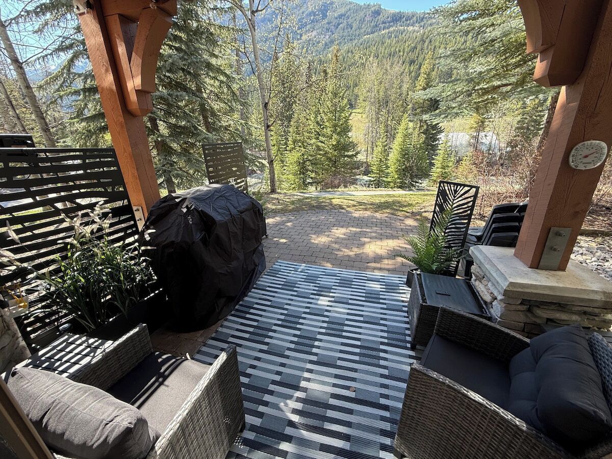 Un patio exterior con suelo a cuadros, mobiliario de mimbre y vistas a una cadena montañosa boscosa.