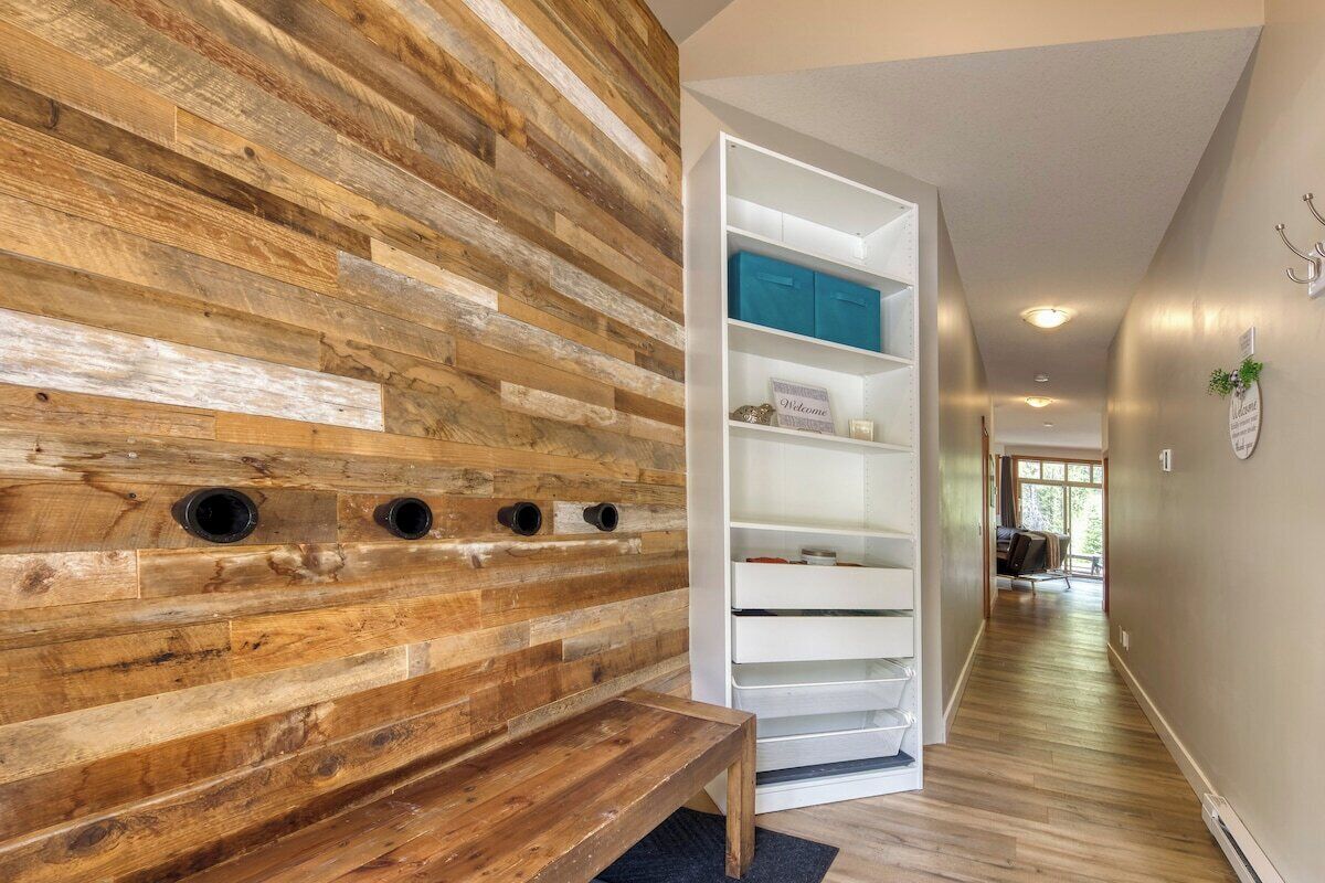 A hallway with a wooden wall, a white shelving unit, and a bench.