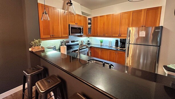 A modern kitchen with wooden cabinets, stainless steel appliances, and a black countertop.