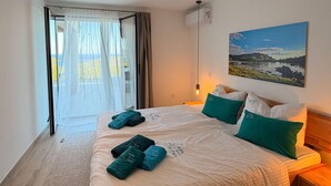A hotel room with a bed, a painting, a window with curtains, and a view of the outdoors. - Casa Trè Fari - Holiday home in Corsica with sea view (Porto-Vecchio)
