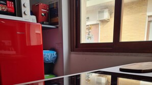 A kitchen with a red refrigerator, a microwave, and a window overlooking a balcony.