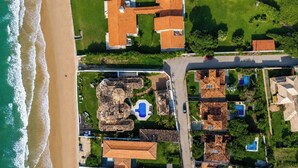 Eine Luftaufnahme eines Küstengrundstücks mit mehreren Gebäuden, einem Pool und einem Strand.