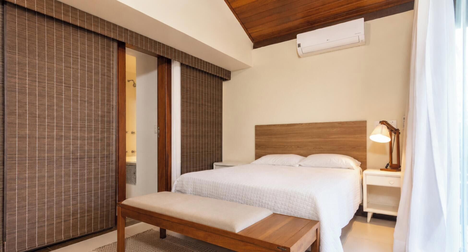 Un dormitorio con cama, mesita de noche, lámpara y un banco.