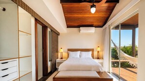 Ein Schlafzimmer mit Holzboden, einem großen Bett mit weißer Bettwäsche, zwei Nachttischlampen und Blick auf Grün hinter einem großen Fenster.