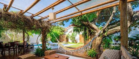 A covered outdoor area with a pool, wooden furniture, and a hammock.