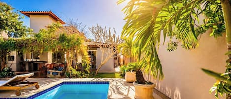 Un patio trasero con piscina, pérgola y diversas plantas.