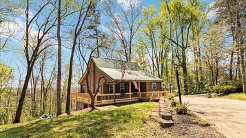 Une cabane en bois dotée d’un porche, entourée d’arbres et baignée par un ciel dégagé.