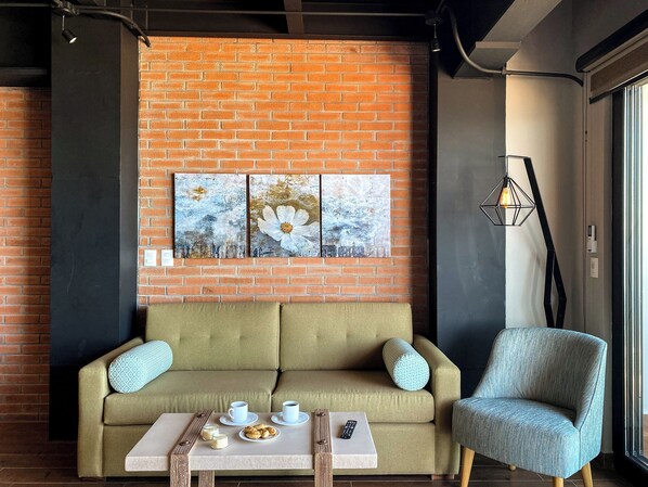 A cozy room with a brick wall, a sofa, a table with cups and pastries, and a chair.