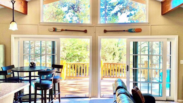 Una habitación amplia con techo alto, ventanas grandes, una zona de comedor con mesa y sillas, y un área de descanso con sofá.