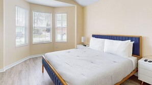 A bedroom with a large bed, a nightstand, and a window with blinds.