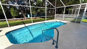 A swimming pool with a metal safety railing, surrounded by a white fence and trees.