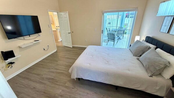 A bedroom with a bed, a TV mounted on the wall, and a balcony with a view.