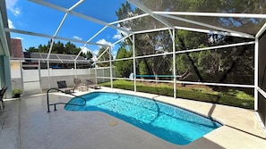 Une piscine dotée d’une enceinte en verre, entourée d’une terrasse avec des chaises et offrant une vue sur les arbres.