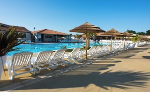Et poolområde med liggestole og parasoller, en klar blå pool og bygninger med tagtægl i baggrunden.