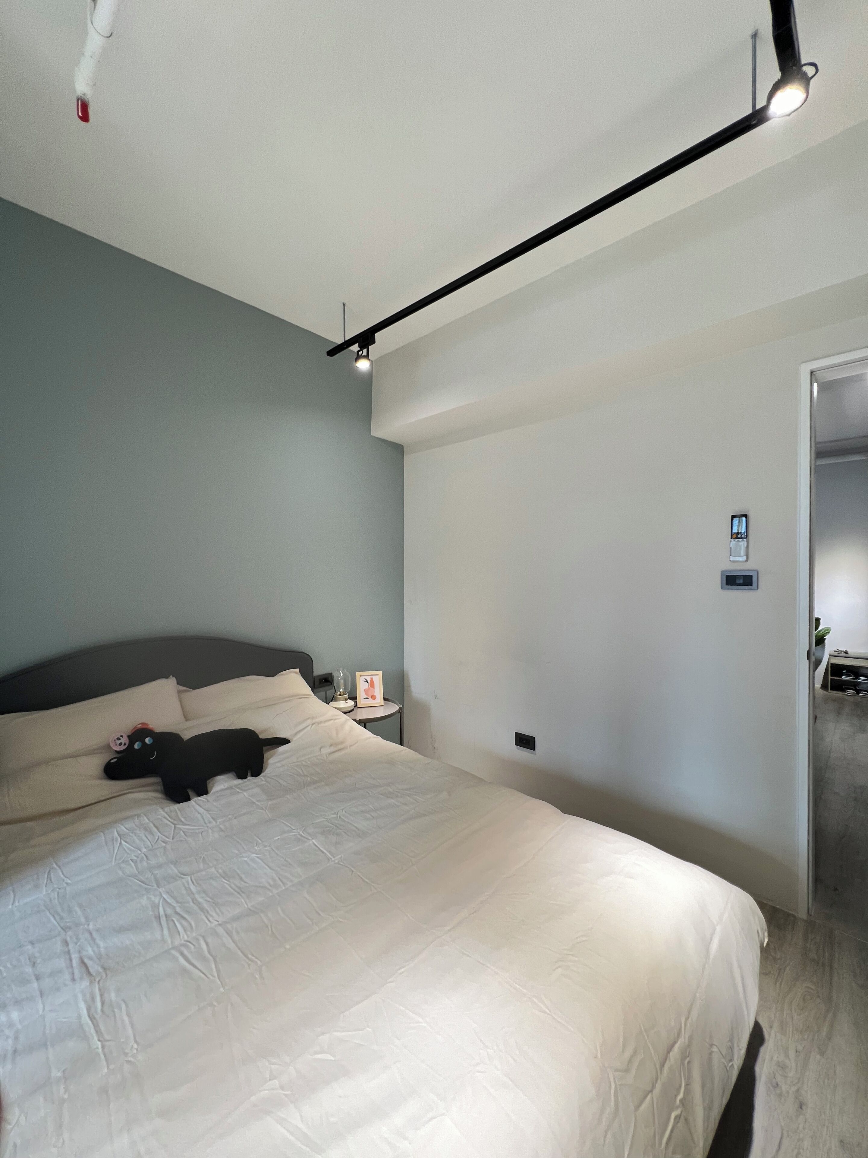 A bedroom with a bed, a nightstand, a wall-mounted light fixture, and a door.