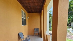 Un espacio al aire libre techado con dos sillas y un banco, techo de madera y pared amarilla.