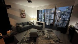 A modern living room with a grey sofa, a matching ottoman, and a patterned rug. A painting is on the wall, and there is a large window with a city view. - Miami Downtown 27 floor Luxe Escape rooftop pool and jacuzzi (Miami)