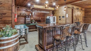 A rustic bar area with wooden walls, metal bar stools, and a refrigerator. - Cozy Longhorn Suite on the River (Granbury)