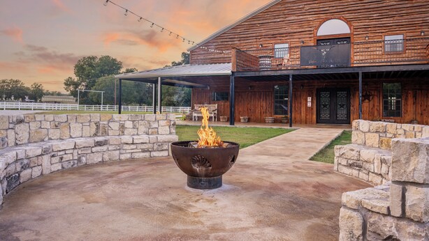 A rustic wooden building with a stone fire pit in the foreground. - Cozy Longhorn Suite on the River (Granbury)