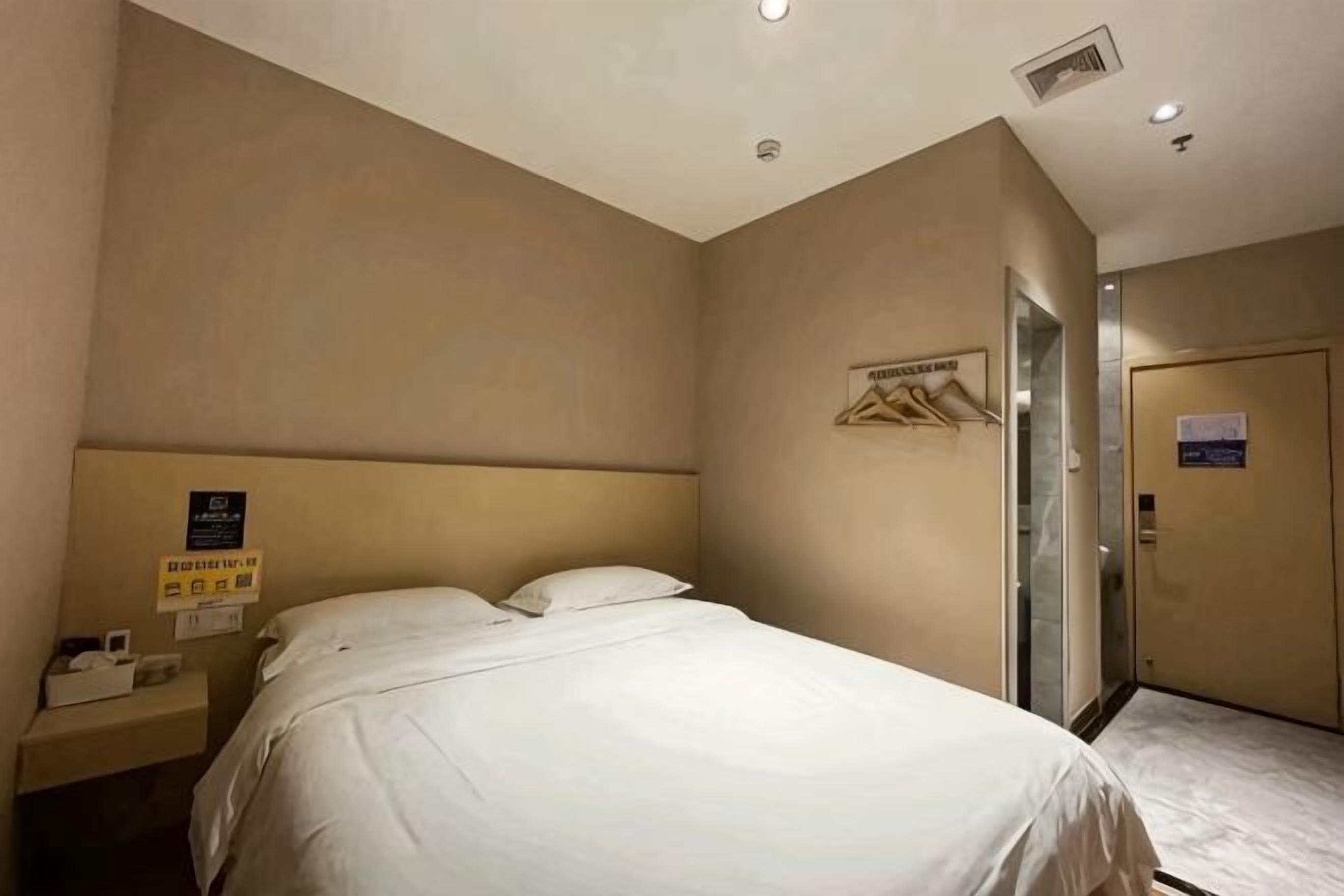 Habitación de hotel con cama, mesita de noche, teléfono en la pared y puerta con acceso a ascensor.