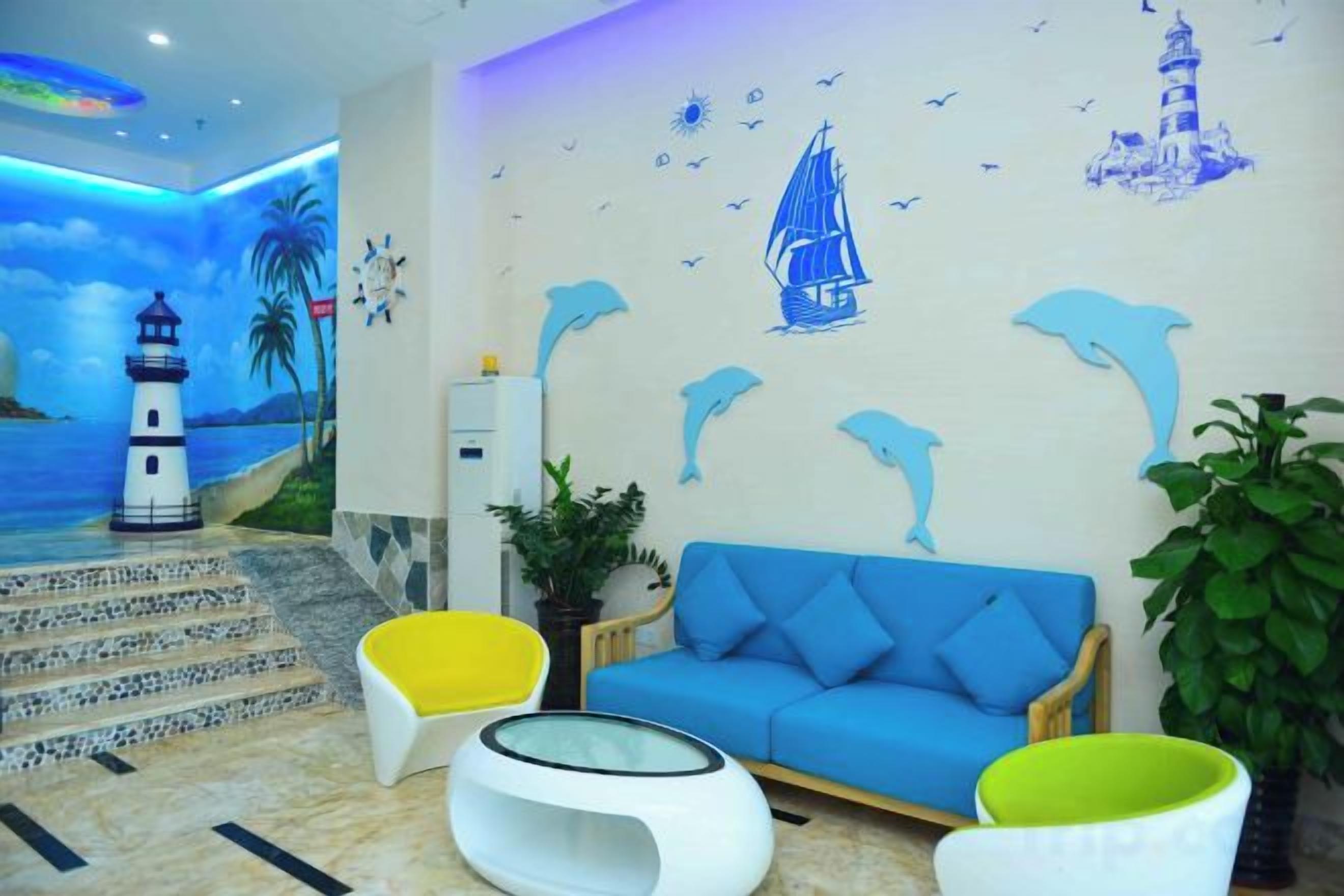 Una habitación con sofá azul, sillas amarillas y blancas, una planta y un mural que muestra un faro y un velero.