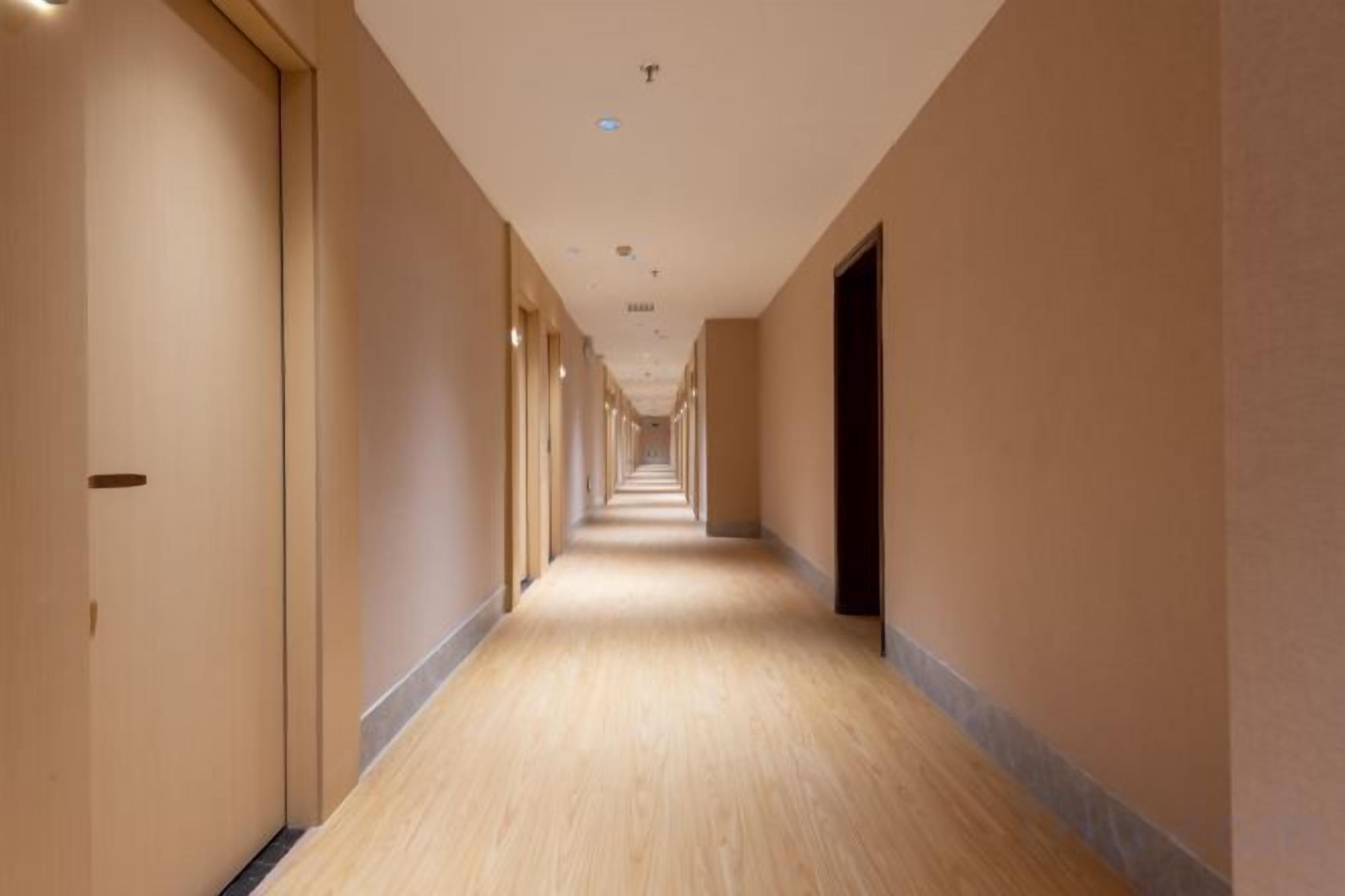 A long, narrow hotel corridor with doors on both sides and a light-colored floor.