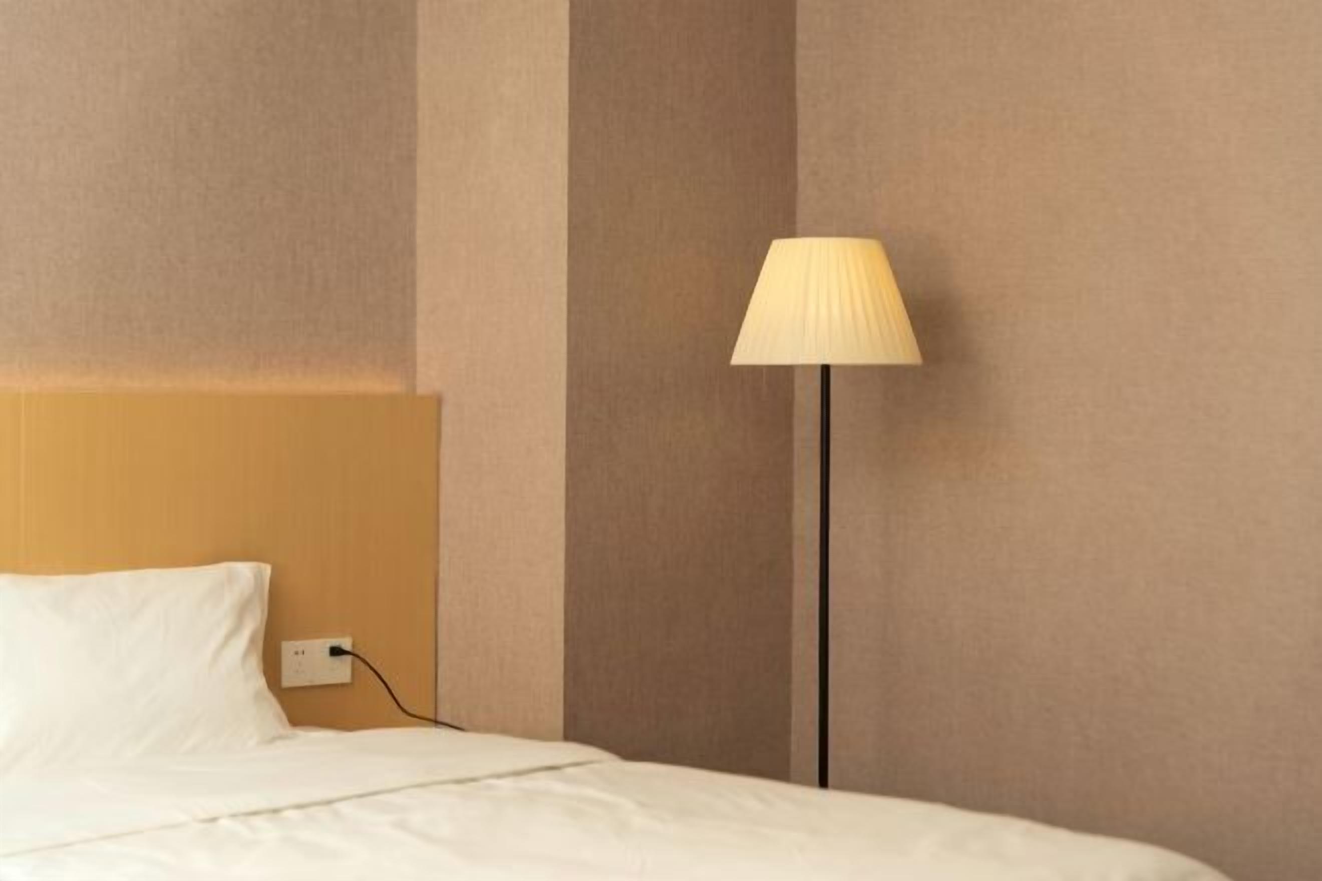 A hotel room with a bed, a nightstand, a lamp, and a wall socket.