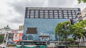 A modern building with a geometric facade, a bus in the foreground, and a traffic light. - Sherlock Apartment (Riyuebei Theater) (Zhuhai)
